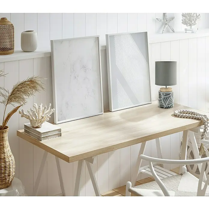 Idp Lampshades Lámpara de sobremesa Vadim - 40 W, L x An x Al: 14 x 14 x 30 cm, Gris, Antracita, E14 - Un interior luminoso y moderno con un escritorio de madera, dos cuadros enmarcados, una lámpara y elementos decorativos, creando un ambiente sereno y elegante.