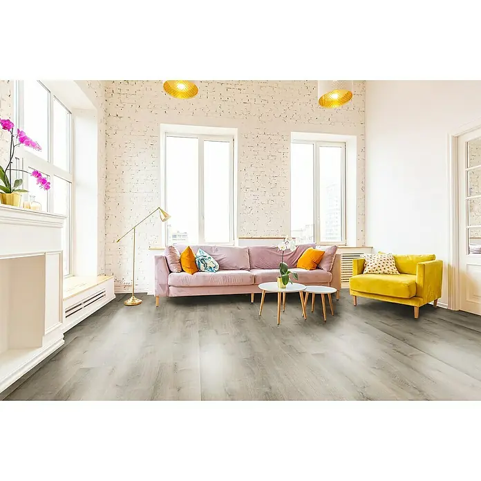 Allure Suelo vinílico SPC Golden Artic - 1.220 x 226 x 6,5 mm, Gris, Resistente al agua - Acogedora sala de estar con elegante suelo de vinilo, un sofá en tonos pastel y un sillón mostaza bajo luces colgantes brillantes.