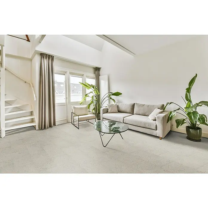 Suelo vinílico SPC Pantheon Stone - 610 x 305 x 5,2 mm - La imagen muestra una sala de estar moderna con un sofá gris, una mesa de centro y plantas de interior. Los colores claros y los elementos naturales crean un ambiente acogedor.