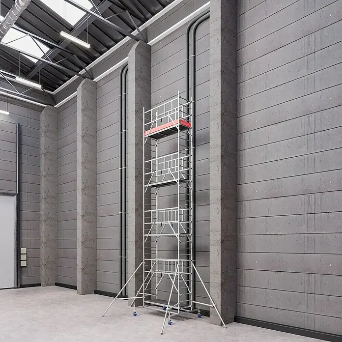 Krause ProTec Rollgerüst - Arbeitshöhe: 9,3 m, Belastbarkeit Plattform: 240 kg - Ein detailreiches Bild eines hohen Baugerüsts aus Metall, das vor einer grauen Betonwand in einer Halle steht.