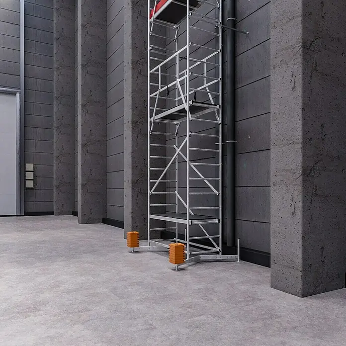 Krause ClimTec Aufstockelement 2. Aufstockung - Arbeitshöhe: 7 m - Ein hoch aufragendes Baugerüst aus Metall steht in einem Raum mit Betonwänden und Stützpfeilern. Es steht auf orangefarbenen Stabilisatoren.