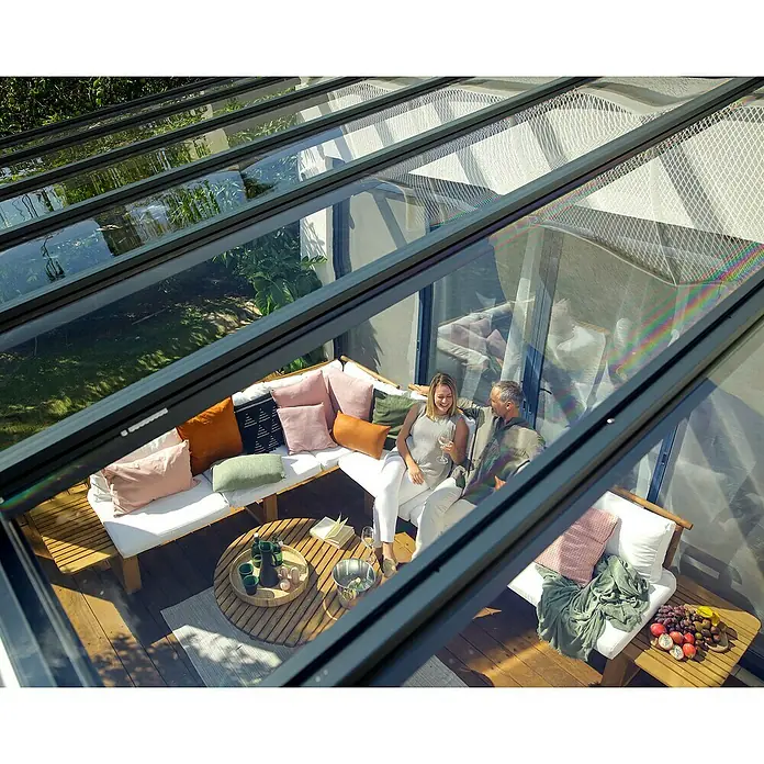 Palram – Canopia Terrassenüberdachung Stockholm - B x T: 515 x 340 cm, Anthrazitgrau, Polycarbonat - Blick von oben auf eine moderne Terrassenüberdachung mit Glasdach, unter der sich eine gemütliche Sitzecke befindet.