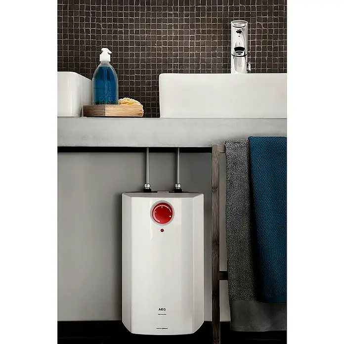 AEG Warmwasserspeicher Huz 5 Drop Stop - 5 l, Temperaturbereich: 35 °C - 85 °C, Untertischmontage - Der AEG Kleinspeicher im Badezimmer. Erwärmt Wasser effizient unter dem Waschbecken mit grauer Keramikfliese im Hintergrund.