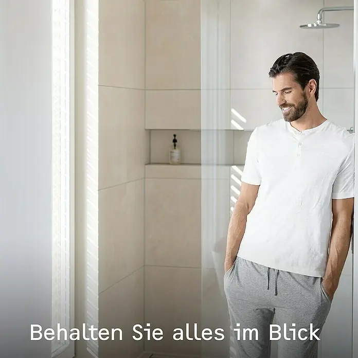 Stiebel Eltron Durchlauferhitzer DHB-E 18 LCD 25A - 18 kW, Elektronisch, Geschlossen - Ein Mann in Alltagskleidung steht in einem modernen Badezimmer mit Duschkopf. Der Fokus liegt auf dem stilvollen und hellen Design des Bads.