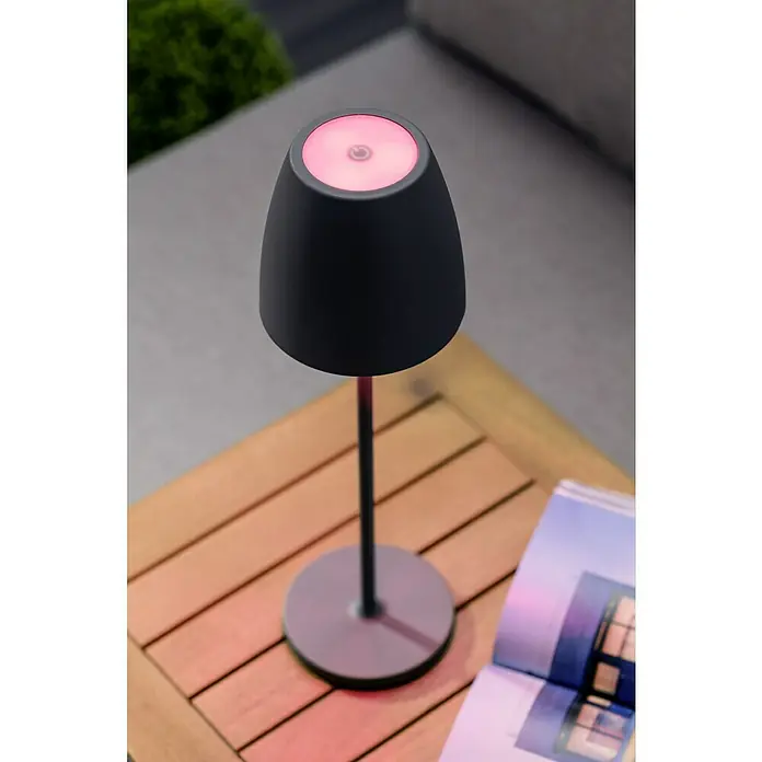 Lavida Akku-Tischleuchte Silea - 3,3 W, Anthrazit, Lichtfarbe: RGBW - Nahaufnahme einer stilvollen, mattschwarzen Tischleuchte mit sanftem, rosa Lichtschein auf einem Holztisch, neben einem aufgeschlagenen Buch.
