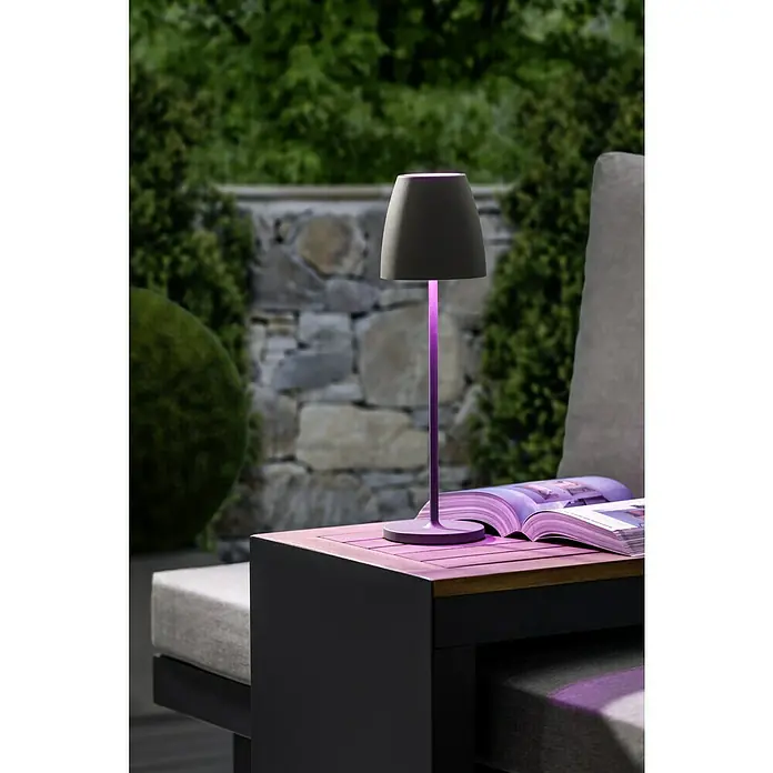 Lavida Akku-Tischleuchte Silea - 3,3 W, Anthrazit, Lichtfarbe: RGBW - Elegante graue Lampe mit violetter Beleuchtung auf einem Tisch im Freien. Die Lampe beleuchtet ein offenes Buch und sorgt für eine stimmungsvolle Atmosphäre.
