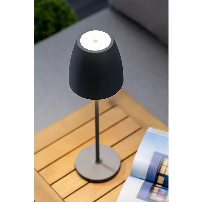 Lavida Akku-Tischleuchte Silea - 3,3 W, Anthrazit, Lichtfarbe: RGBW - Nahaufnahme einer modernen, grauen Tischleuchte auf einem Holztisch mit einem aufgeschlagenen Buch. Perfekt für gemütliche Abende.