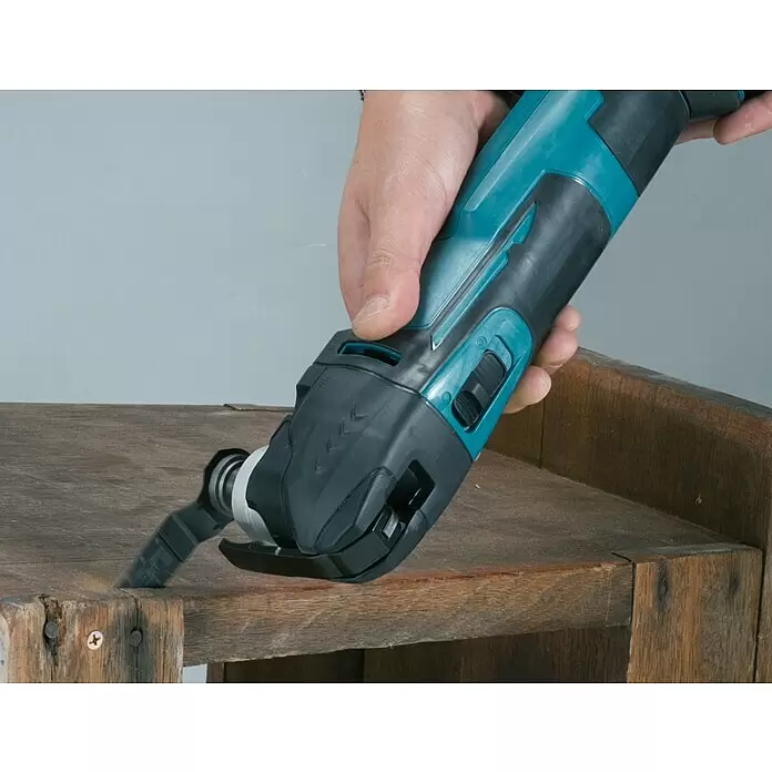 Makita LXT 18V Akku-Rotationswerkzeug DTM51Z - 18 V, Li-Ionen, Ohne Akku - Türkis-schwarzes oszillierendes Multifunktionswerkzeug, das von einer Hand gehalten wird und eine alte Holzoberfläche bearbeitet.