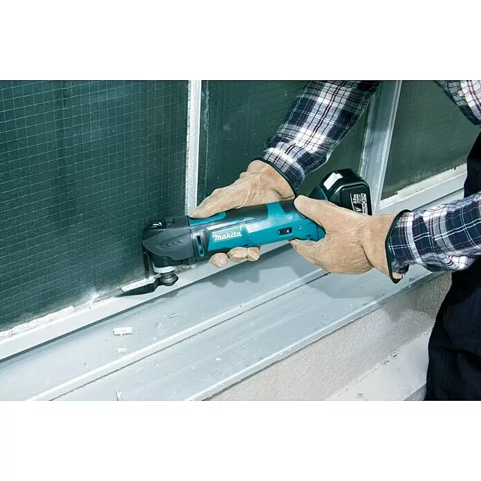 Makita LXT 18V Akku-Rotationswerkzeug DTM51Z - 18 V, Li-Ionen, Ohne Akku - Kabelloses, türkis-schwarzes Makita Multifunktionswerkzeug, von behandschuhten Händen an einem Fensterrahmen verwendet.