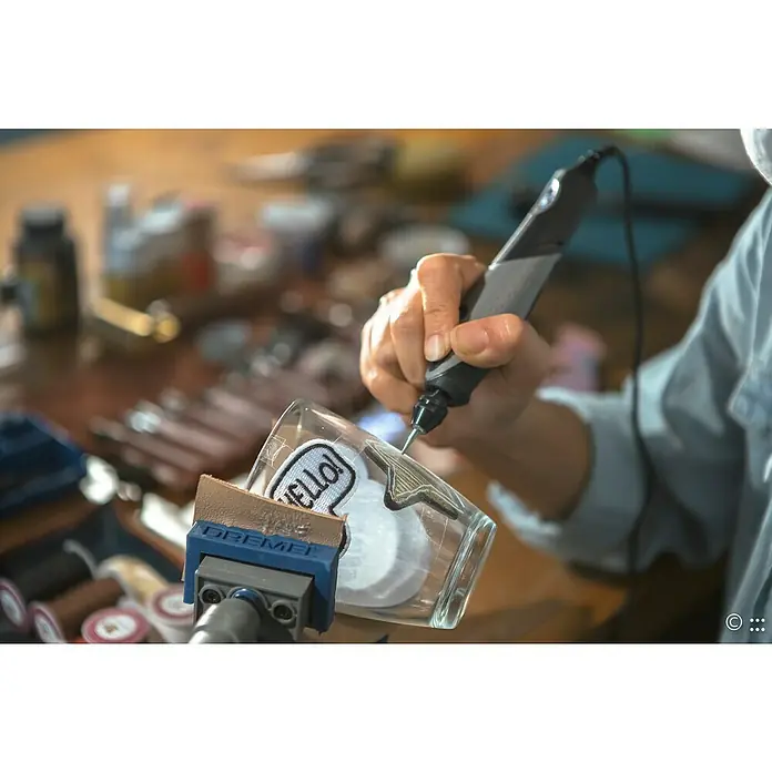 Dremel Elektro-Multifunktionswerkzeug 2050 Stylo+ - 9 W - Eine Nahaufnahme eines Dremel-Werkzeugs, das zum Gravieren eines Glasbechers mit einem "HELLO!"-Aufkleber verwendet wird.