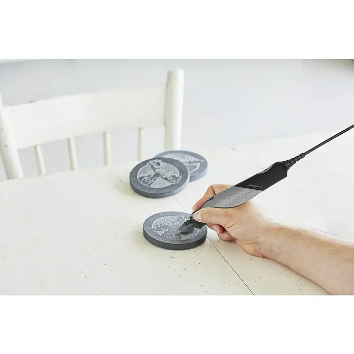 Dremel Elektro-Multifunktionswerkzeug 2050 Stylo+ - 9 W - Nahaufnahme eines Gravierwerkzeugs in der Hand, das für Detailarbeiten auf runden Steinen mit Designs verwendet wird.
