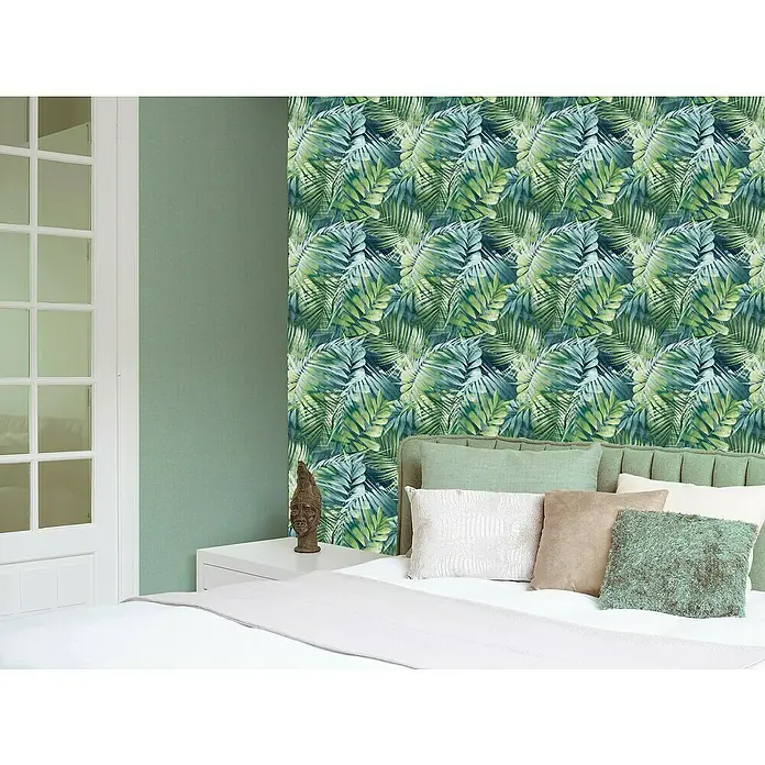 Papel pintado Botánico - Azul, Motivo decorativo, 10 x 0,53 m - Primer plano de un dormitorio exuberante con un vibrante papel pintado de hojas tropicales, complementado con una selección de cojines decorativos y una mesita de noche blanca.