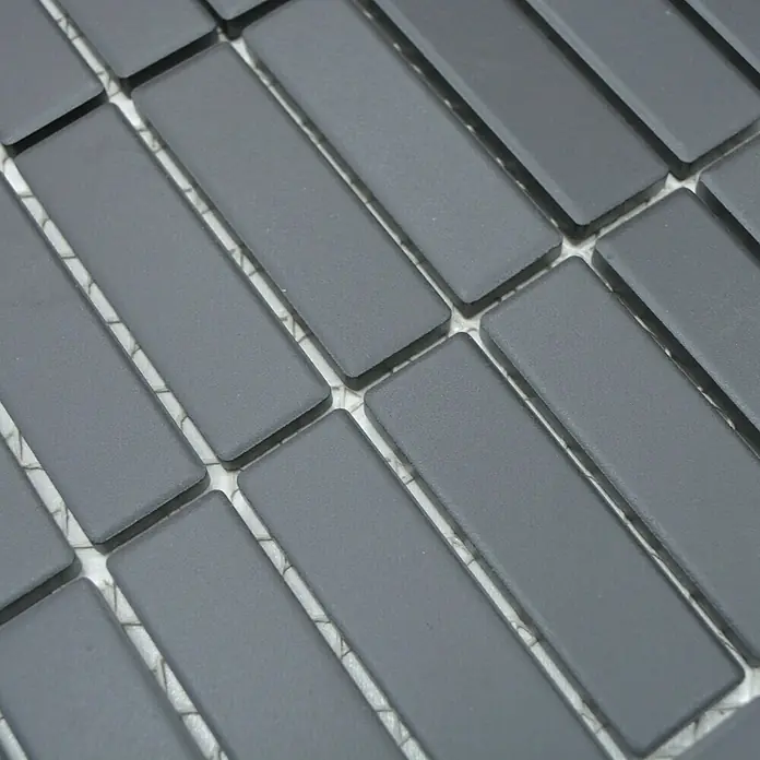 Mosaikfliese Stäbchen Uni CU ST 021 - 29,7 x 29 cm, Schwarz, Matt - Detailaufnahme einer Matte aus länglichen, grauen Mosaikfliesen, die in einem Fischgrätenmuster angeordnet sind. Ideal für stilvolle Wand- und Bodengestaltung.