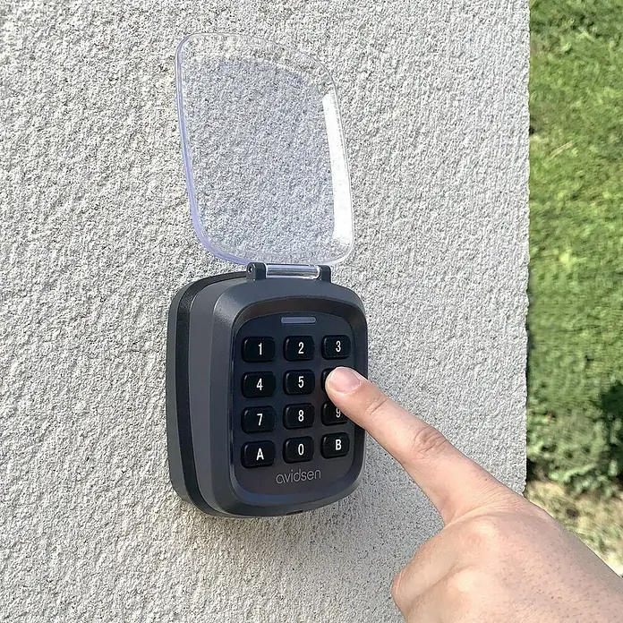Avidsen Teclado de código inalámbrico - Alcance: 80 m - Un teclado Avidsen con una persona presionando un botón, ideal para un acceso seguro. Construcción duradera con tapa de protección contra la intemperie.