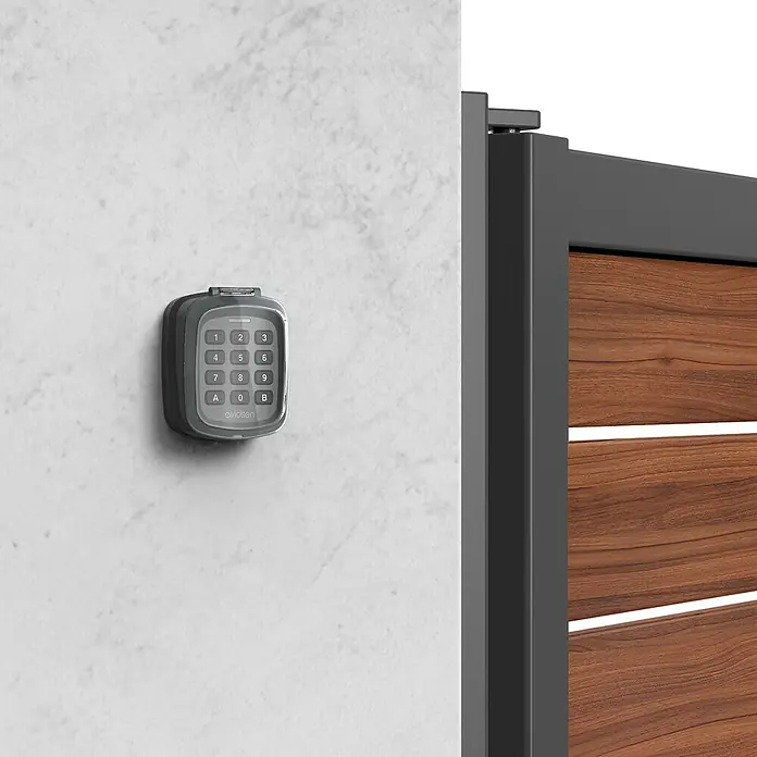 Avidsen Teclado de código inalámbrico - Alcance: 80 m - Vista del producto de una carcasa de teclado Avidsen montada en una pared junto a una valla, lo que garantiza una mayor seguridad y control de acceso.