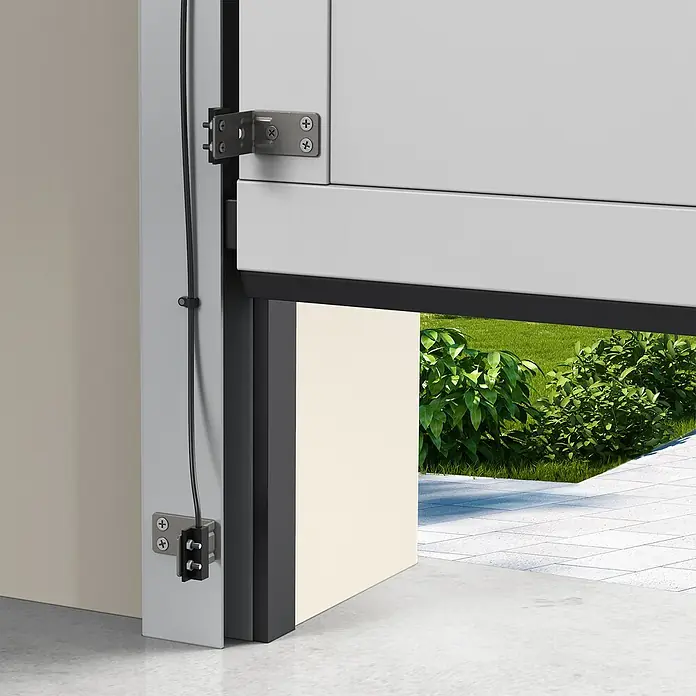 Avidsen Módulo de comando inalámbrico WiFi - 50 m - Primer plano de una puerta de garaje abierta que ofrece una vista de plantas verdes y un suelo de piedra. La construcción de la puerta es claramente visible.