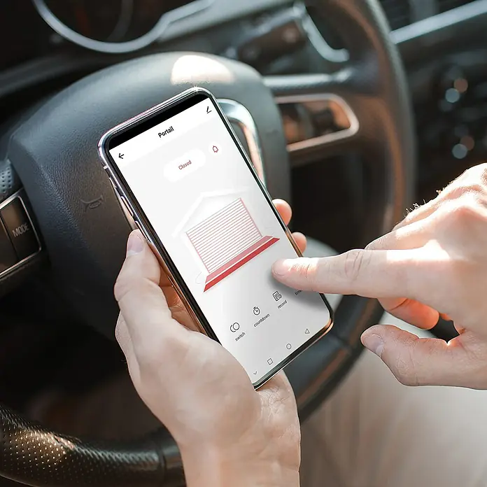 Avidsen Módulo de comando inalámbrico WiFi - 50 m - Primer plano de un teléfono inteligente sostenido en un coche, que muestra una aplicación para controlar una puerta de garaje.