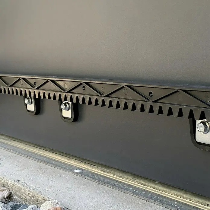 Avidsen Mecanismo de puerta de garaje Zenia 250 - Anchura puerta: 0 m - 4 m, 24 W - Primer plano de una cremallera negra con pernos fijada a una superficie gris.