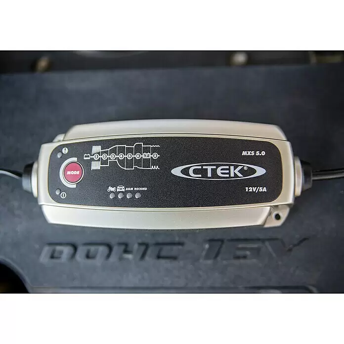 CTEK Automatik-Ladegerät MXS 7.0 - Ladestrom: 7,2 A, Kapazität: 14 Ah - 150 Ah - Silber-schwarzes CTEK MXS 5.0 Batterieladegerät mit Anzeigeleuchten, an ein Fahrzeug angeschlossen.