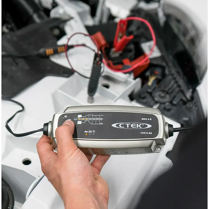 CTEK Automatik-Ladegerät MXS 3.8 EU - Ladestrom: 3,8 A, Kapazität: 1,2 Ah - 80 Ah - Ein CTEK MXS 3.8 Batterieladegerät wird vor dem Hintergrund eines Motorraums bedient.