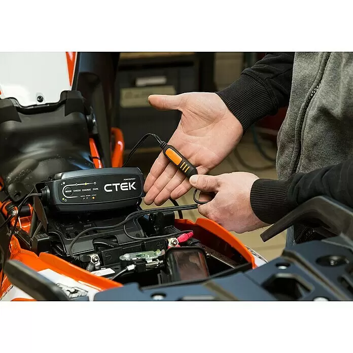 CTEK Automatik-Ladegerät CT5 Powersport EU - Kapazität: 5 Ah - 25 Ah - Eine Person schließt ein schwarzes CTEK Powersport Ladegerät mit orangefarbenen Akzenten an eine Motorradbatterie an.