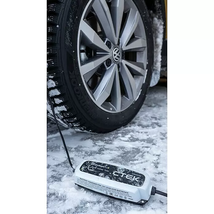 CTEK Automatik-Ladegerät CT5 START/STOP EU - Kapazität: 14 Ah - 130 Ah - Weiß-schwarzes CTEK Batterieladegerät auf Schnee neben einem Autorad, deutet auf Laden bei Kälte hin.