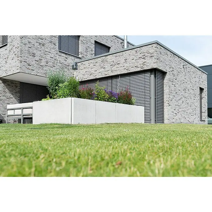 Diephaus L-Stein Slim - 130 cm, 100 cm, Stärke: 8 cm, Grau - Ein rechteckiger, weißer Betonblumenkasten vor einem modernen Haus mit Ziegelmauerwerk, gefüllt mit grünen Pflanzen und bunten Blumen.