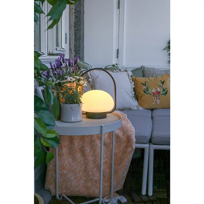 Nordlux Sponge Mobiles Licht To Go - 4,8 W, Schwarz, Weiß, Höhe: 27,7 cm, IP65, Warmweiß - Diese stimmungsvolle Szene zeigt eine moderne Lampe, die auf einem Beistelltisch neben einer Pflanze und einem gemütlichen Sofa platziert ist.