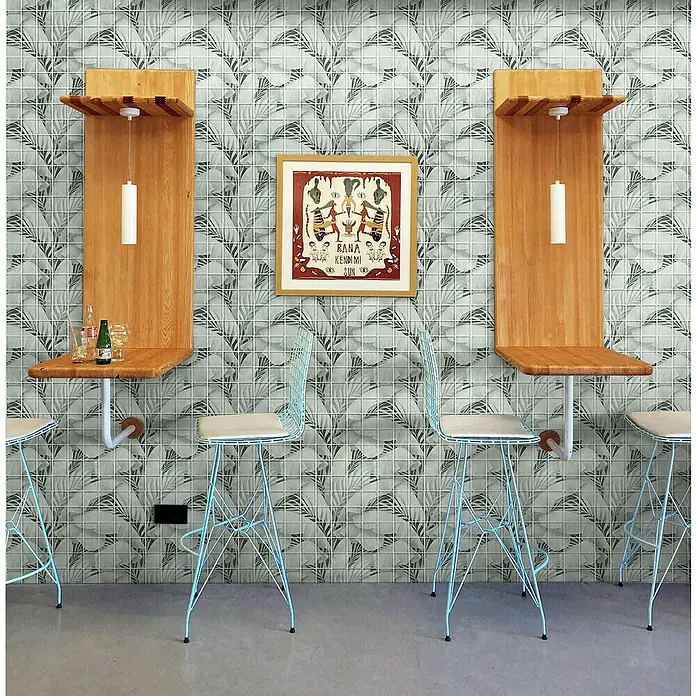 Mosaikfliese Quadrat Crystal Rainforest XCM RF03 - 29,8 x 29,8 cm, Grau, Glänzend - Elegantes Interieur mit hellblauen Barhockern, Holztischen und einem gerahmten Kunstwerk an einer stilvollen Wand mit Blattmuster.