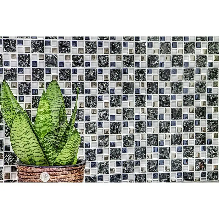 Mosaikfliese Crystal Mix XIC K1499 - 33,8 x 33,8 cm, Schwarz, Glänzend - Nahaufnahme einer Sansevieria-Pflanze im Topf vor einem Hintergrund aus Mosaikfliesen in Schwarz, Weiß und Silber.