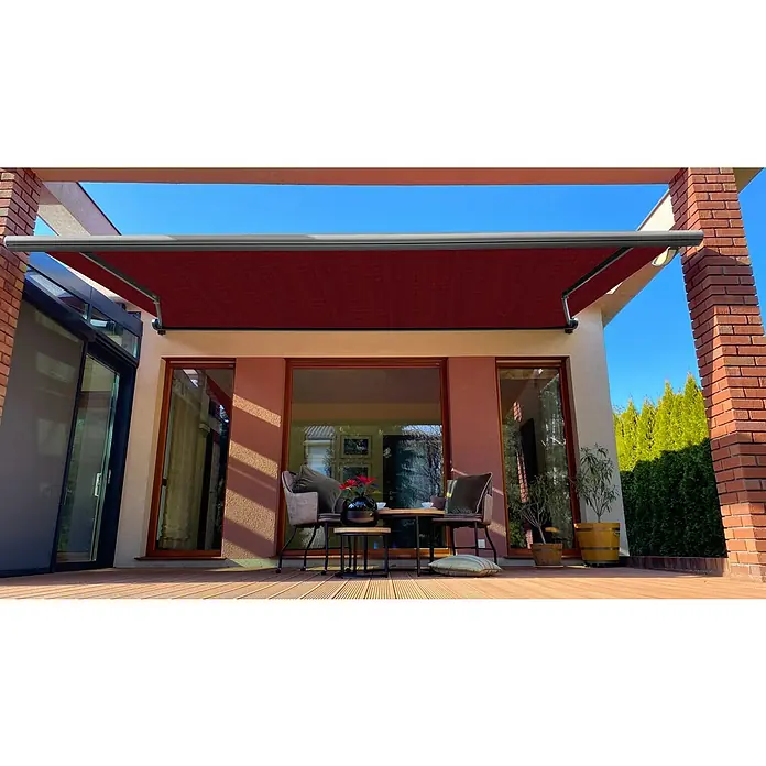 SM Vollkassettenmarkise T-407/11Rot, Farbe Gestell: Weißaluminum, Breite: 3,6 m, Ausfall: 2,5 m - Außenansicht einer Terrasse mit einer rotbraunen Markise, die Schatten spendet und einen gemütlichen Sitzbereich mit Tisch und Stühlen schafft.