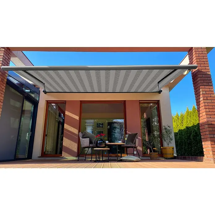 SM Vollkassettenmarkise REC-089 - Hellgrau/Grau, Farbe Gestell: Weißaluminum, Breite: 3,6 m, Ausfall: 2,5 m - Eine graue Markise mit Streifenmuster spendet Schatten über einer Terrasse mit Terrassendielen und Sitzbereich.