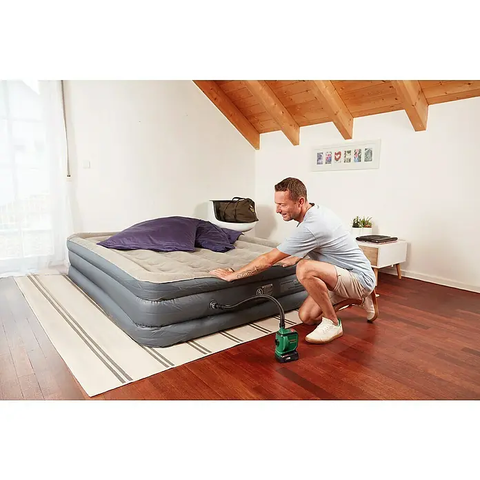 Bosch Power for All 18V Akku-Luftpumpe EasyInflate 18V-500 - 18 V, 1 Akku - Ein Mann pumpt eine graue Luftmatratze mit einer grünen elektrischen Pumpe in einem Zimmer mit Holzboden auf.
