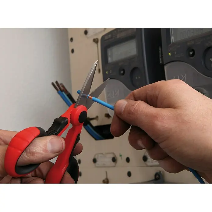 Super Ego Tijeras de trabajo para electricistas - Largo: 14,4 cm, Longitud de corte: 42 mm, Rojo/Negro - Cortando un cable eléctrico azul con unas tijeras rojas frente a un panel eléctrico.
