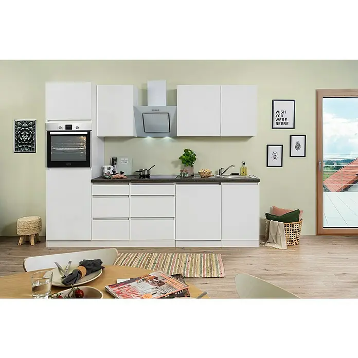 Respekta Premium Küchenleerblock LorenaBreite: 280 cm, Weiß, Matt, Dekor Arbeitsplatte: Steinoptik, Ohne Elektrogeräte - Eine moderne Küche mit weißen Schränken, dunkler Arbeitsplatte, eingebautem Ofen und einem Esstisch mit Gedeck im Vordergrund.