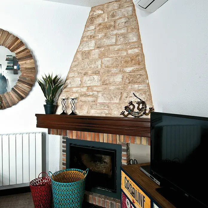 Revestimiento de piedra Silleria Cobre - Cobre, Cantidad total: 4 pzs. - Interior de sala de estar con chimenea revestida de piedra rústica y elementos decorativos como un espejo y cestas.