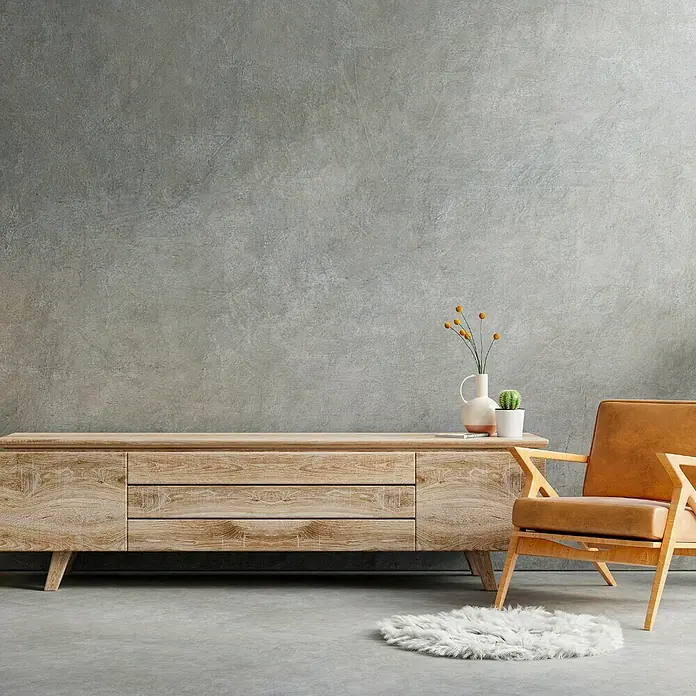 Fleur Kit Microcemento - Greige, 2 kg - Decoración moderna de salón con mueble de madera clara, sillón y decoraciones minimalistas sobre una pared de hormigón gris.