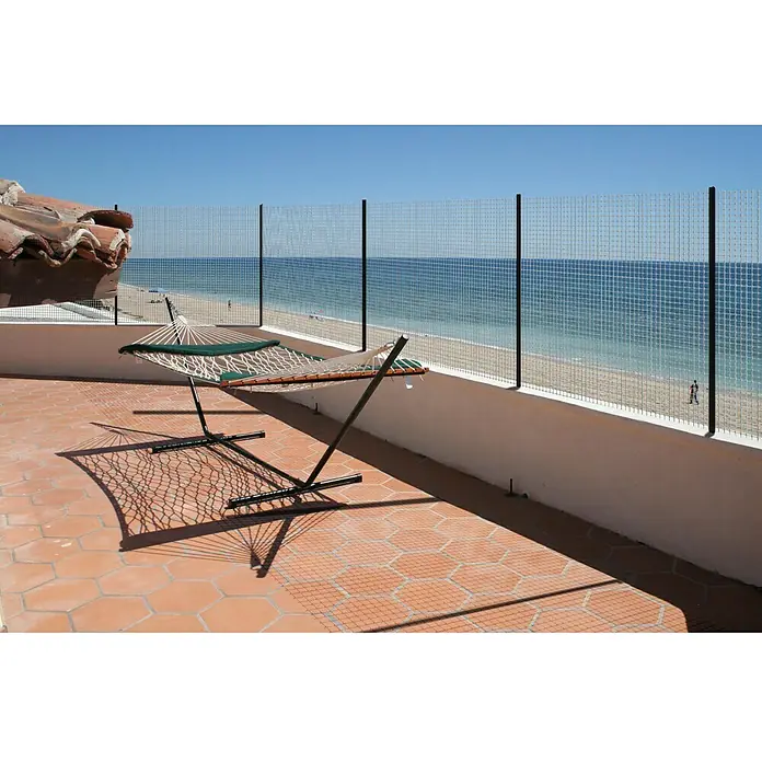 Malla protectora Millenium - Verde, L x Al: 10 x 1,5 m - Primer plano de una hamaca con soporte en una terraza con vista al mar, que invita a la relajación.