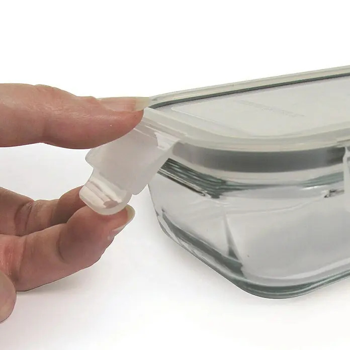 Set de recipientes de almacenaje con tapa hermética - 3 ud., Material: Vidrio - Primer plano de un recipiente de vidrio transparente con un cierre transparente que está siendo abierto por una mano. El recipiente es rectangular y limpio.