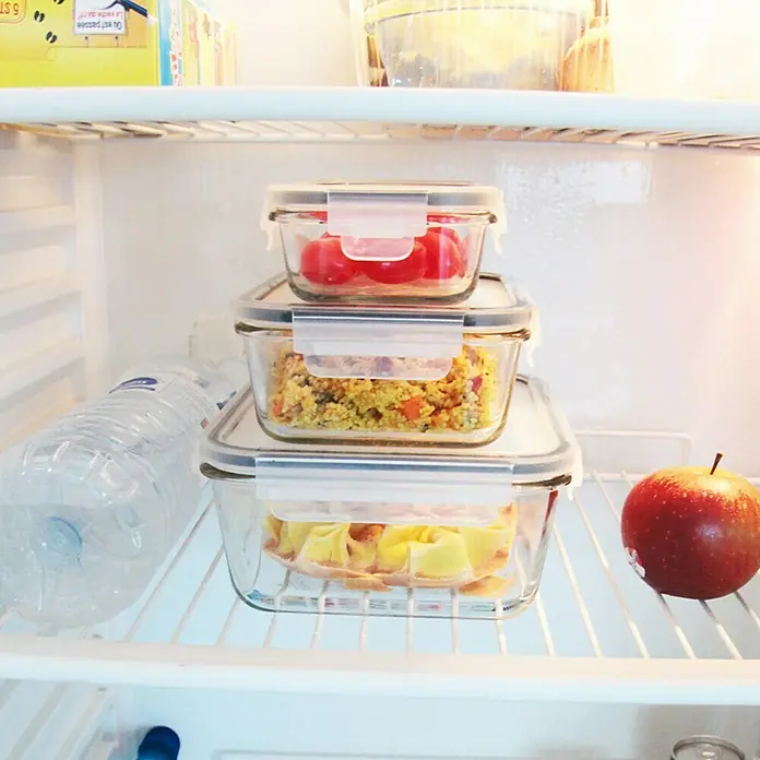 Set de recipientes de almacenaje con tapa hermética - 3 ud., Material: Vidrio - Frigorífico con tres recipientes de vidrio apilados llenos de alimentos frescos, una botella de agua y una manzana.