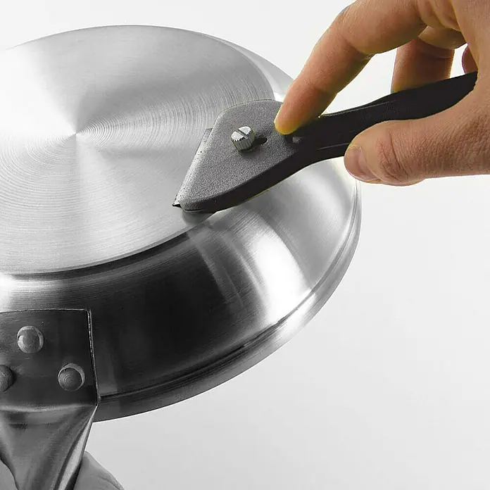 Rascador para vitrocerámica - Largo: 13,9 cm, Específico para: Placas de cocina - Primer plano de un rascador que se utiliza para limpiar una sartén de acero inoxidable, eliminando residuos persistentes.