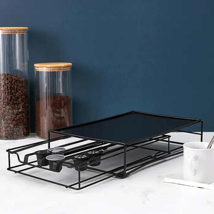 Dispensador cápsulas de café Nespresso - L x An x Al: 31 x 21 x 7 cm, 32 cápsulas - Un almacén de cápsulas de café negro con cajón sobre una superficie blanca, junto a recipientes de café y una taza.