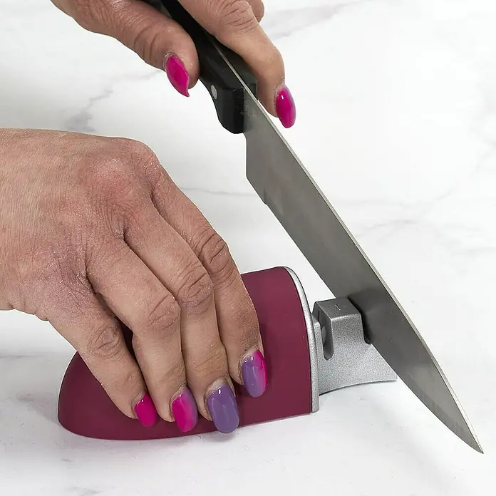 Afilador de cuchillos de hoja de acero - Específico para: Cuchillos con hoja de acero, Variado - Una persona afilando un cuchillo con un afilador rojo y plateado sobre una superficie blanca.