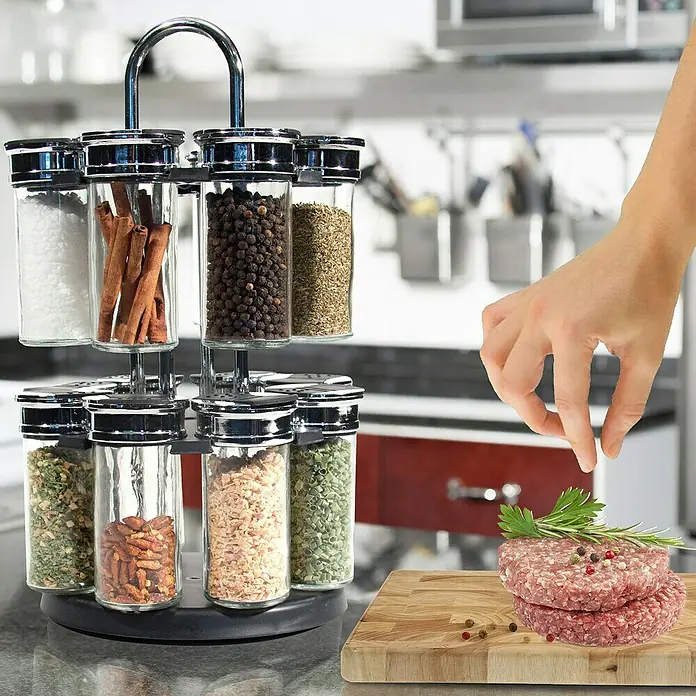 Especiero carrusel giratorio - Específico para: 16 botes, Ø x Al: 19 mm x 31,5 cm - Especiero giratorio lleno de especias variadas junto a carne picada en una tabla de cortar y una mano agregando especias.