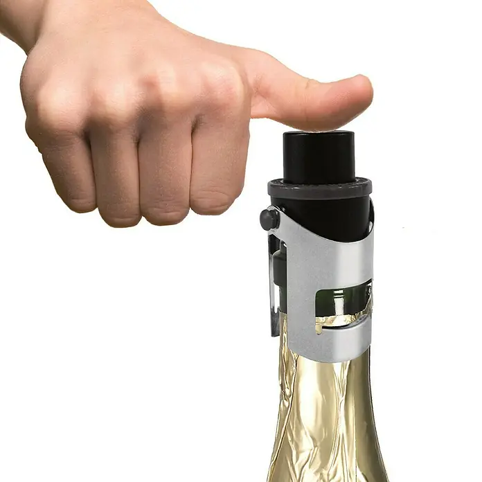Tapón de botella Cava Air Pump - Ø x Al: 3,5 x 8 cm, Específico para: Cava - Una mano presiona un tapón de champán fijado a una botella envuelta en papel de aluminio dorado. Ideal para abrir botellas de vino espumoso de forma segura.