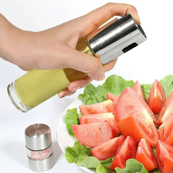 Pulverizador de aceite - Ø x Al: 4,2 x 18 cm, 100 ml - Una mano rocía una ensalada con tomates con un rociador de aceite. Al lado hay un molinillo de sal, complementando la ensalada.