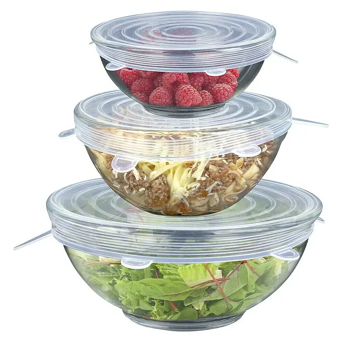 Set de tapas flexibles - 3 ud., Silicona - Cuencos de vidrio apilados con tapas de silicona estirables en diferentes tamaños llenos de frambuesas, ensalada y un plato de carne.