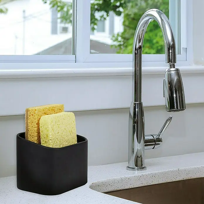 Cesta para la esponja de cocina - L x An x Al: 8 x 8 x 10 cm, Plástico - Organizador de fregadero negro con esponjas amarillas junto a un grifo moderno sobre una encimera de cocina luminosa.