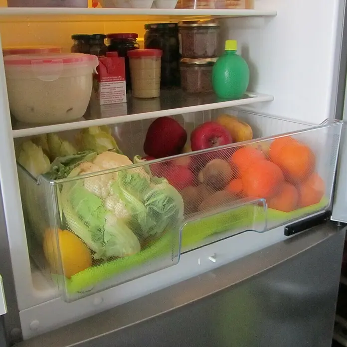 Alfombrilla de protección para nevera - 30 x 47 cm, Poliuretano - Vislumbre del interior de un refrigerador, que revela un cajón transparente lleno de frutas y verduras frescas, como lechuga, coliflor y naranjas.