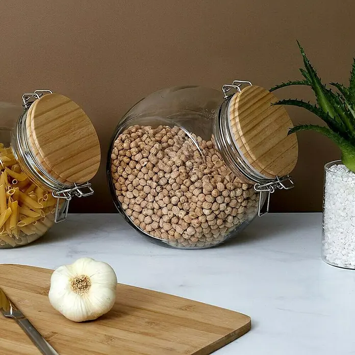 Frasco con cierre mecánico - Vidrio, 2,2 l - Frascos de vidrio con pasta y garbanzos, complementados con un diente de ajo sobre una tabla de cortar.